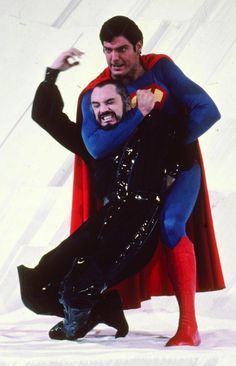 two men dressed as superman and the man in black is holding another man's head