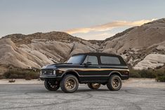 the black truck is parked in front of some rocks and mountains, with an orange light shining on it