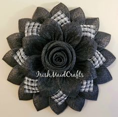 a large black and white flower with plaid ribbon on the center is mounted on a wall