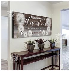 this is us wood sign with two potted plants on the table in front of it