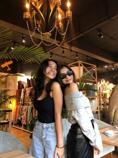 two women standing next to each other in front of a chandelier with lights