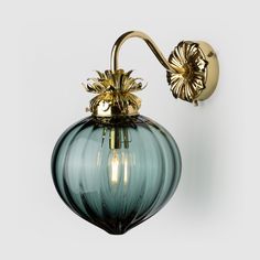 a green glass wall light with a gold metal arm and flower decoration on the side