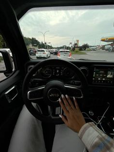 a person driving a car on a busy street with other cars in the background and one hand on the steering wheel