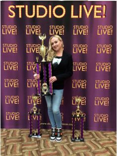 a woman standing next to two trophies in front of a purple backdrop with the words studio live on it