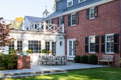 a brick house with white trim and black shutters on the windows is surrounded by lush green grass