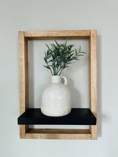 a white vase sitting on top of a wooden shelf next to a wall mounted plant