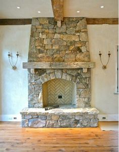 a stone fireplace in the middle of a room with wood flooring and exposed beams