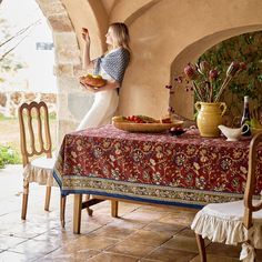 a woman sitting at a table with food on it and flowers in vases next to her