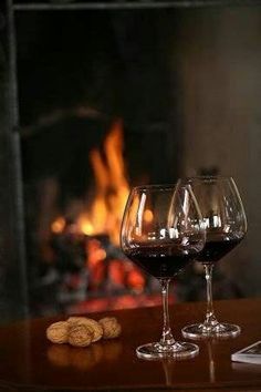 two wine glasses sitting on top of a table next to a tabletop with a fireplace in the background