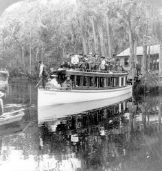 an old black and white photo of a boat full of people on the water with trees in the background