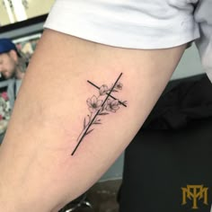 a cross and flowers tattoo on the left arm by an unknown person's leg