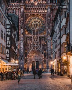 people are walking around in an old european city at night with lights on the buildings