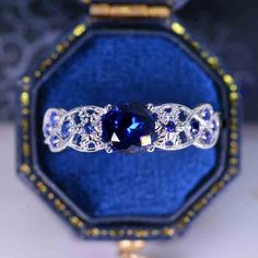 a blue and white diamond ring sitting in a velvet box with gold trimmings