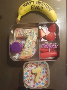 a birthday cake in a container with a banana on the top and other food items