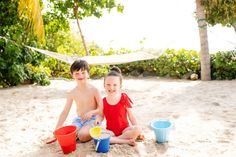 two children sitting in the sand with buckets and cups