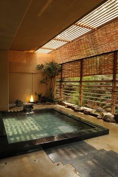 an indoor swimming pool surrounded by rocks and bamboo screens with a lamp on the side