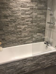 a bath tub sitting next to a shower head in a bathroom with grey tile on the walls