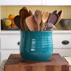 a teal cup filled with wooden spoons and utensils on top of a cutting board