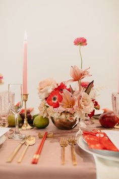 the table is set with pink flowers and gold cutlery, silverware and candles