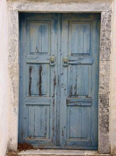 two blue doors are open in an old stone building with grass growing on the ground