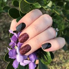 a woman's hand with black and white nail polish on her nails next to purple flowers