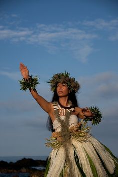 a woman wearing a grass skirt and flower headdress with her hands in the air