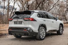 the rear end of a white toyota rav parked in front of some bare trees