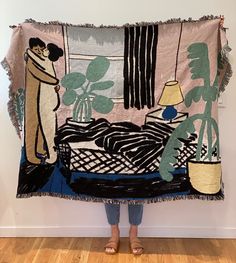 a woman is holding up a tapestry with an image of a bed and plants on it