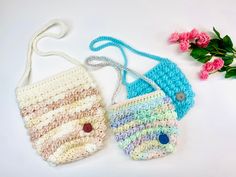 two crocheted purses sitting on top of a table next to pink flowers