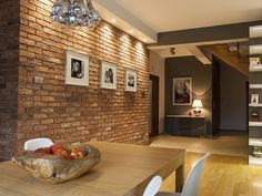 a dining room table with chairs and a bowl of fruit on top of it in front of a brick wall