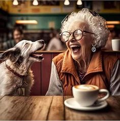 an older woman laughing while sitting at a table next to a dog with its mouth open