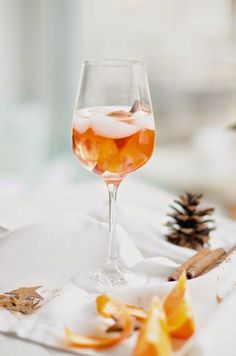 a glass of wine sitting on top of a table next to an orange slice and pine cone