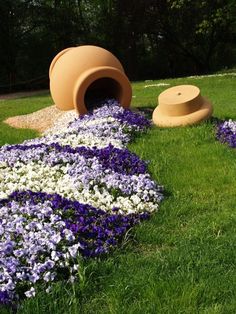 purple and white flowers are in the grass next to a large potted planter