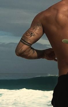 a man holding a surfboard in his right hand and looking at the ocean from behind him