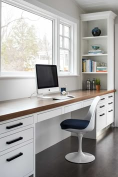 a desk with a computer on top of it next to a bookshelf and window