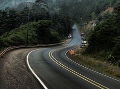 an empty road in the mountains with trees on both sides and cars driving down it