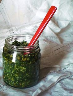 a glass jar filled with green pestle on top of a white table cloth next to a red plastic spoon