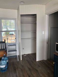 an empty room with white walls and wood flooring in the foreground is a ladder leading up to a window