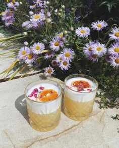 two glasses filled with drinks sitting next to purple flowers