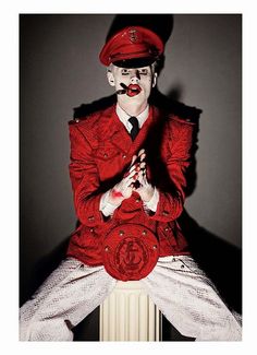 a man dressed as a clown sitting on top of a radiator with his hands in his pockets