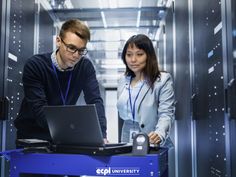 two people in a server room looking at a laptop