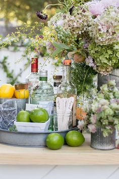 an assortment of alcohol bottles, lemons and limes on a table with flowers