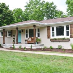 a white house with brown shutters on the front and side windows, grass in front