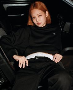 a woman sitting in the back of a car wearing black pants and a turtle neck sweater