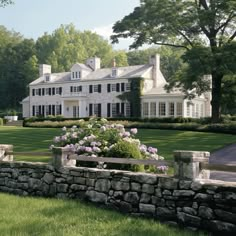 a large white house sitting on top of a lush green field next to a stone wall