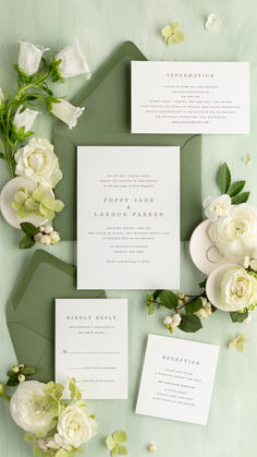 the wedding stationery is laid out on top of green envelopes and white flowers