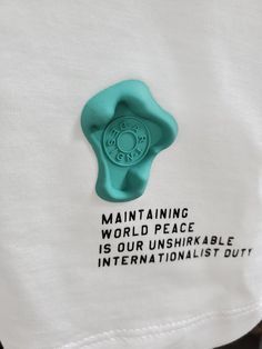 a white t - shirt with a green button that says maintaining world peace is our unshirkable internationalist duty