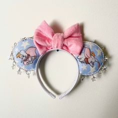 A handmade, original set of Minnie Ears with fabric depicting the Dumbo collection. A pink, cotton bow is placed within the center with dangling, clear stars draped around the ears.  Size: Adult  Weight: Light Color: Blue and Pink  Can make custom order's based on any fabric and beading with similar fabric or idea. Dumbo Ears, Disney Mickey Ears, Disney Merch, Minnie Mouse Ears, Disney Ears, Minnie Ears, Turban Headbands, Mickey Ears, Disney Fun