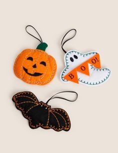 three halloween ornaments are hanging from strings on a white surface, one has a bat and the other is a pumpkin