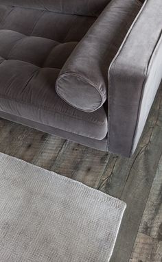 a gray couch sitting on top of a wooden floor next to a rug and table